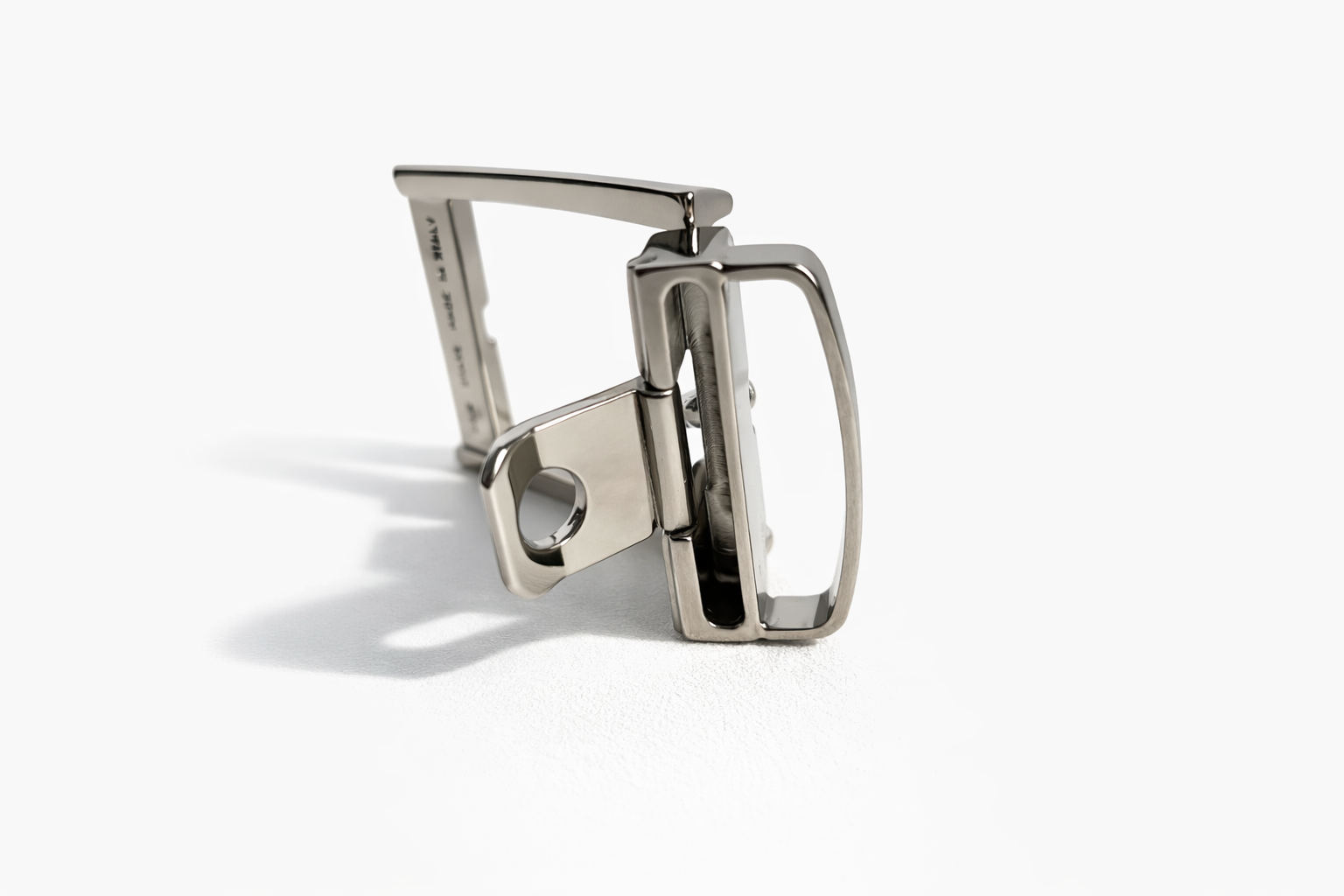 attacco-per-fibbia-sganciabile Attacco per fibbia sganciabile in metallo argentato lucido con leva e foro di aggancio, ripreso su sfondo bianco con ombra naturale che evidenzia il meccanismo di apertura.